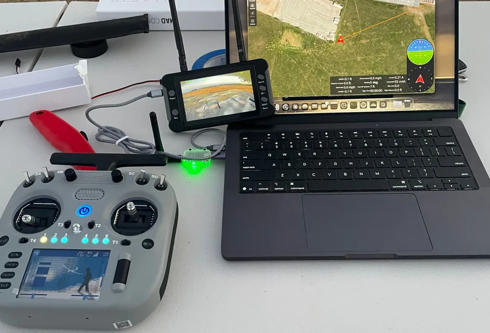 A ground station on a field table: a transmitter, an FPV monitor and a laptop running mission planning software over a satellite map.